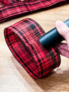 a person is holding a red and black plaid ribbon on a wooden surface with other items in the background