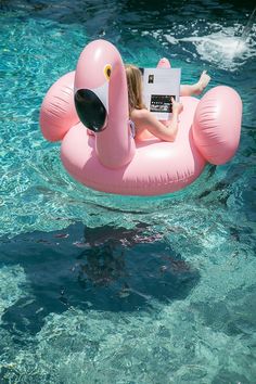 a woman is sitting on an inflatable flamingo with a laptop while floating in the water