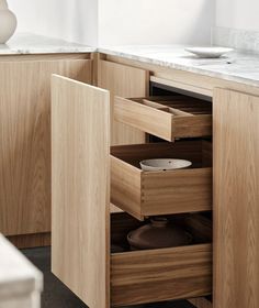 an open drawer in a kitchen with marble counter tops and wooden cabinetry, along with a white bowl on the side