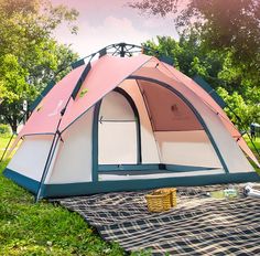 a pink and white tent sitting on top of a blanket in the grass next to trees