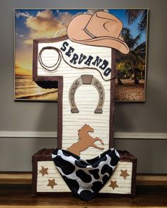 a wooden sign with a cow print bandana on it and a cowboy hat hanging from the top