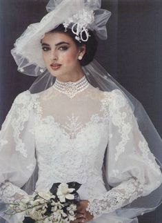 a woman in a wedding dress and veil with flowers on her head is holding a bouquet