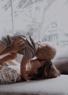 a mother kissing her daughter on the cheek while lying on a couch in front of a window