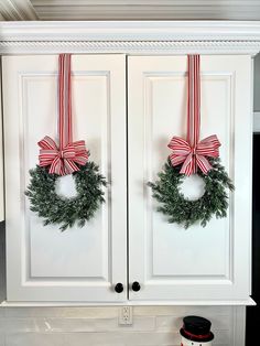 two wreaths hanging on the back of white cupboards with red and white ribbons