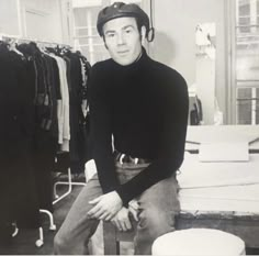 a black and white photo of a man sitting on a stool in a clothing store