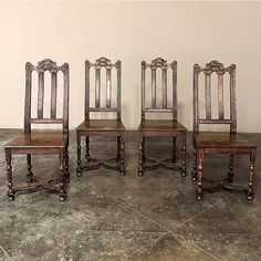 four wooden chairs sitting next to each other on top of a tile floor in front of a white wall