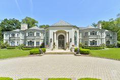 a large white house in the middle of a lush green yard with hedges and bushes