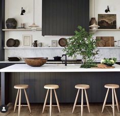 three stools sit in front of an island with plants and bowls on the counter