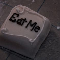 a cake with the word eat me on it sitting on a tiled floor next to a knife