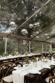 the tables are set up for an outdoor wedding reception with clear glass walls and hanging lights