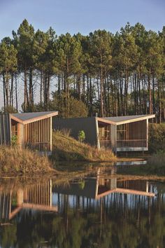 two wooden cabins sitting on top of a lush green hillside next to a body of water