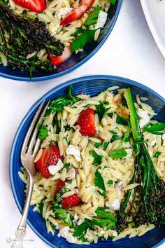 two blue plates filled with pasta and strawberries on top of a white tablecloth