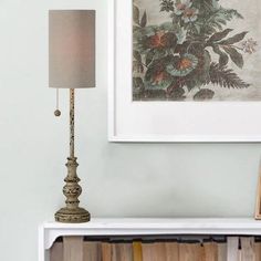 a white bookcase with books and a lamp on top of it next to a painting