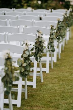 rows of white chairs with greenery on them