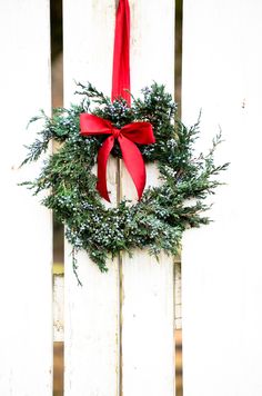 a wreath hanging on the side of a white fence with a red ribbon around it