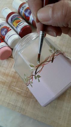 a person holding a pen in their hand near some paint bottles on a wooden table