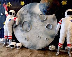 two astronauts standing next to an artificial moon