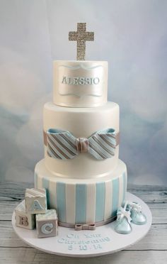 a three tiered cake decorated with blue and white stripes, baby shoes, and a cross