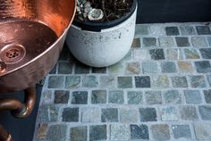 a potted plant sitting on top of a stone floor next to a copper sink