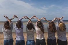 four girls are standing in front of the ocean and making heart shapes with their hands