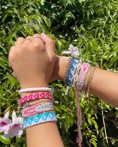 two girls are holding their hands together with bracelets on each hand and flowers in the background