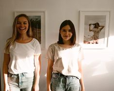 two young women standing next to each other in front of pictures on the wall behind them