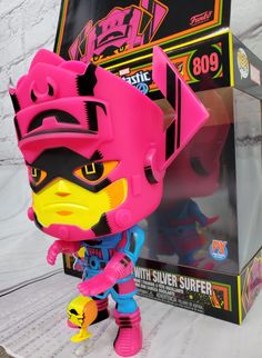 a pink and yellow action figure in front of a black box with graffiti on it