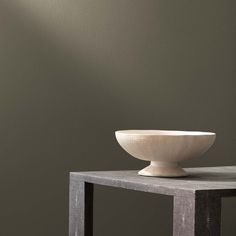 a white bowl sitting on top of a table next to a gray wall and chair