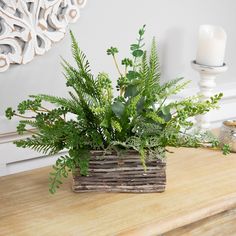 a basket filled with green plants sitting on top of a wooden table next to a candle