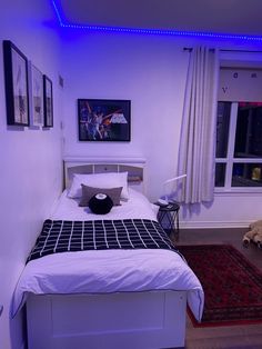 a white bed sitting in a bedroom next to a window with blue lights on it