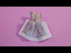 an origami doll made out of money sitting on top of a pink surface