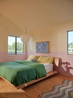 a bedroom with pink walls and green bedspread on the bed is next to a large window