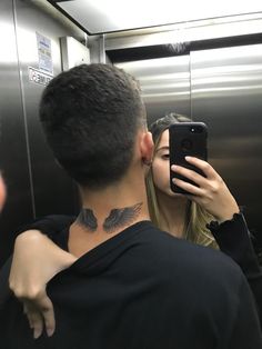 a man and woman taking a selfie in an elevator with tattoos on their neck