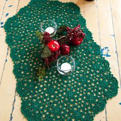 two apples and some berries on a green doily with white candlesticks next to them