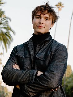 a man with his arms crossed standing in front of palm trees