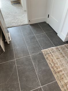 a grey tile floor in a house with stairs and rugs on the ground next to it