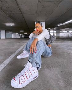 a woman sitting on the ground with her foot up in front of her face and wearing white sneakers