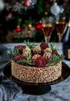 there is a cake with berries and pine cones on the table next to a bottle of wine