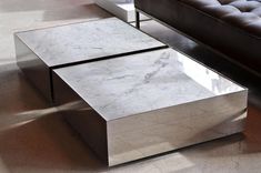 a marble coffee table sitting on top of a floor next to a brown leather couch