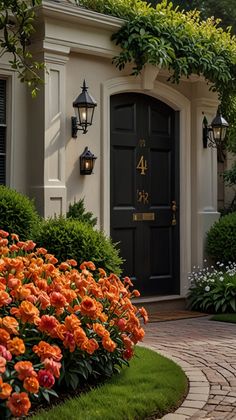 an orange flower bed in front of a black door and some green bushes with flowers