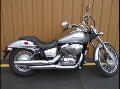 a silver motorcycle parked in front of a brown metal wall with yellow lines on it