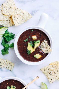 two bowls of black bean soup with tortilla chips and avocado on the side