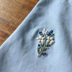 a blue shirt with white flowers embroidered on the front and back, sitting on a wooden surface