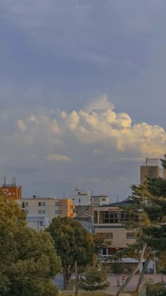 an airplane is flying in the sky over some trees and buildings on a cloudy day