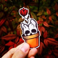 a hand holding a sticker with two skulls in a flower pot