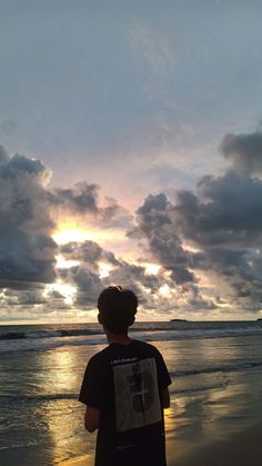 a man standing on top of a beach next to the ocean under a cloudy sky