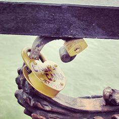 the lock is attached to an ornate iron fence with water in the backround