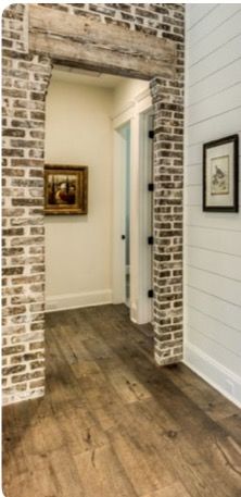 an empty hallway with brick walls and wood flooring, framed pictures on the wall