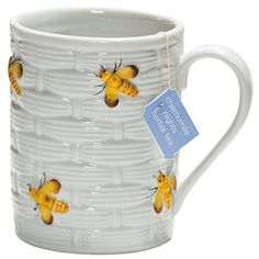 a white mug with yellow bees on it and a blue tag hanging from the handle