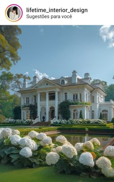 a large white house with lots of flowers in the front yard and landscaping around it